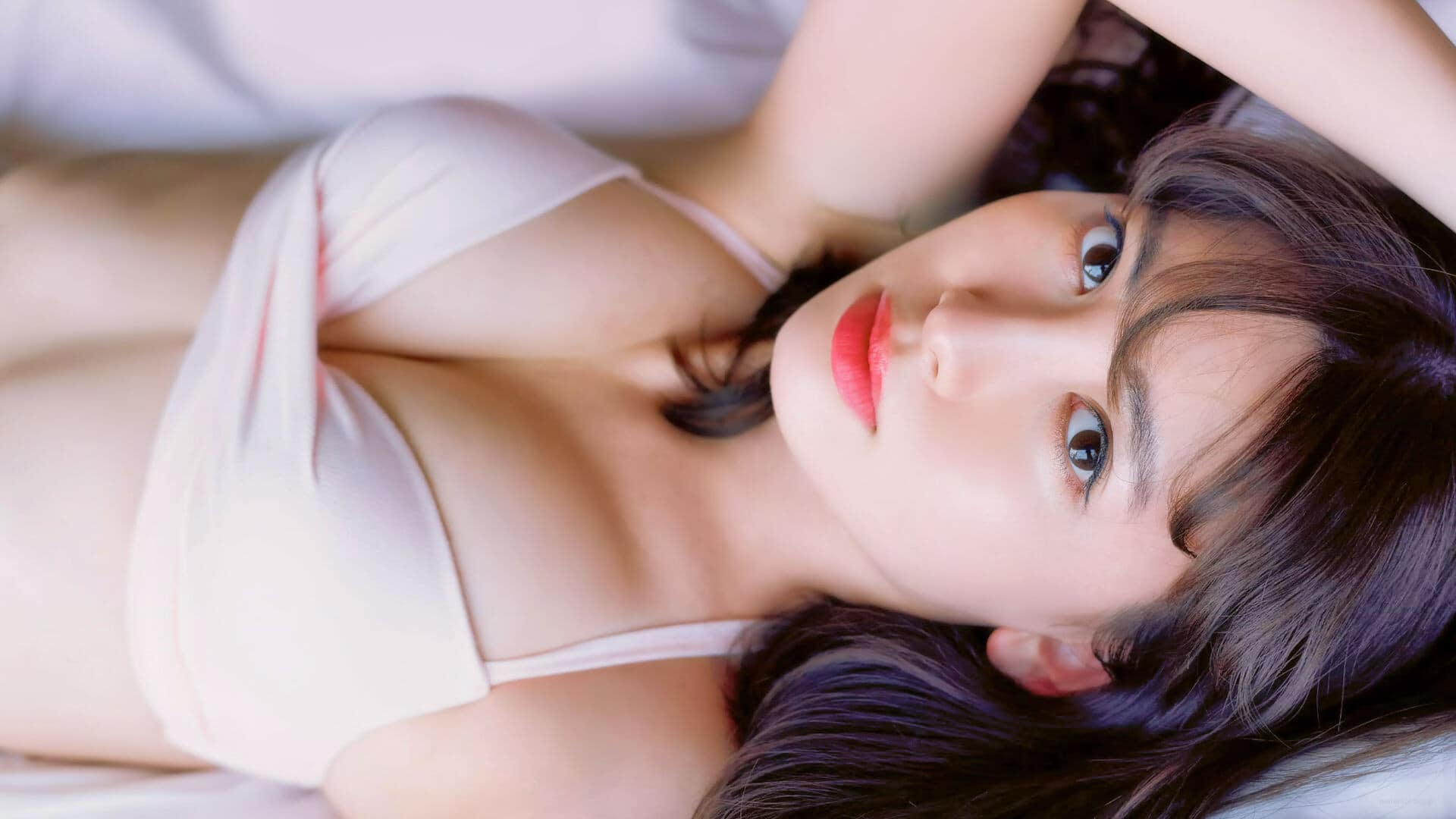 Alluring Asian brunette in swimsuit on bed wallpaper.
