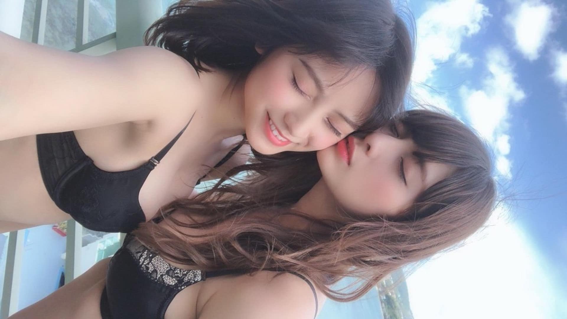 Attractive Asian lesbian couple in swimsuits poolside.