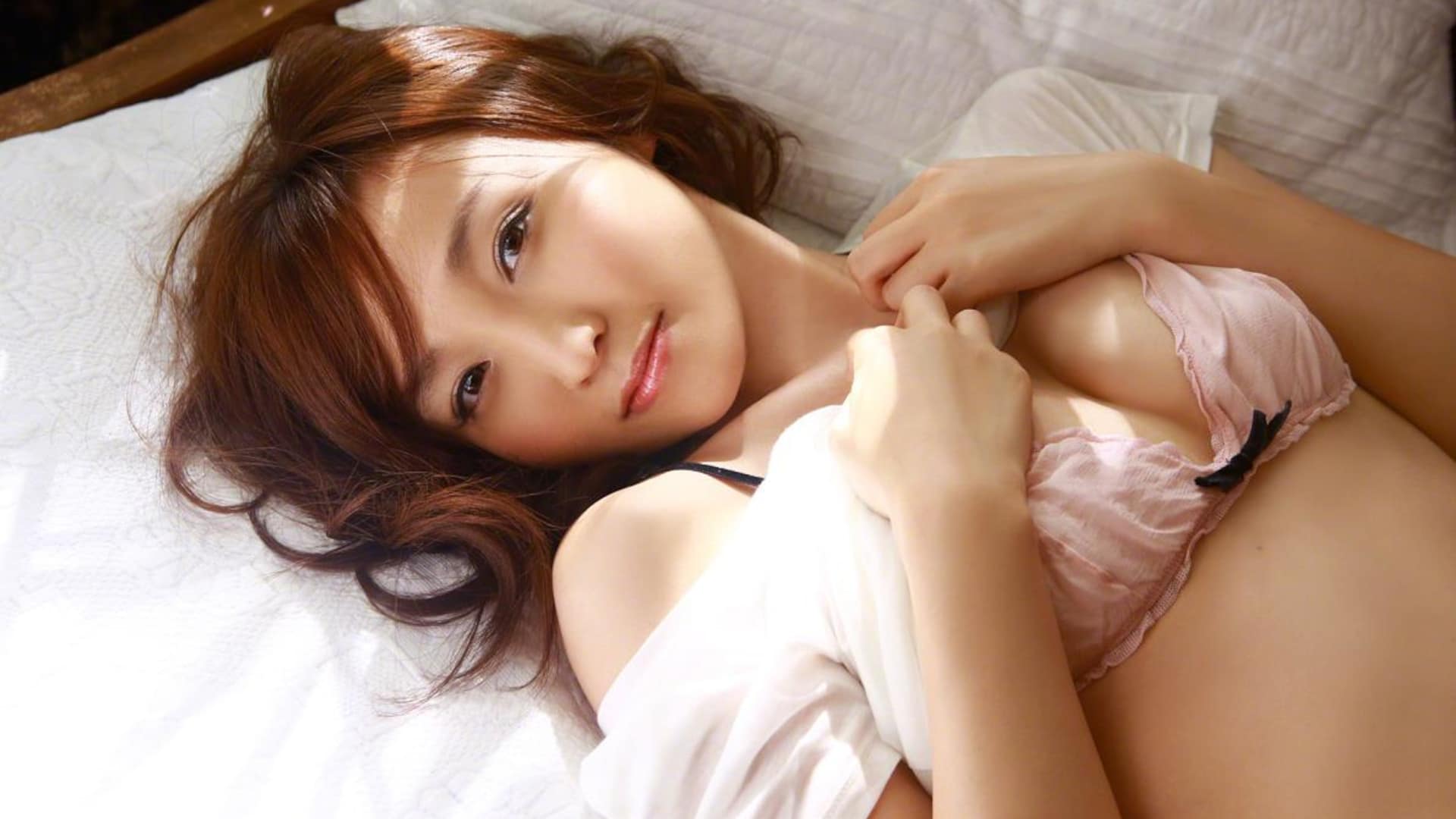 Captivating Asian woman with fiery red hair in elegant lingerie on a luxurious bed.