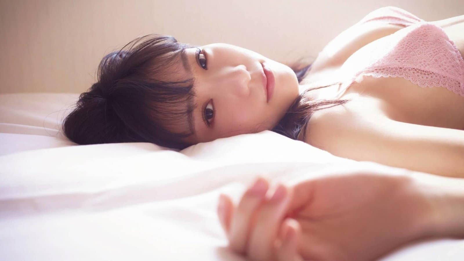 Brunette Asian woman in elegant lingerie relaxing on a bed, perfect for a captivating wallpaper download.