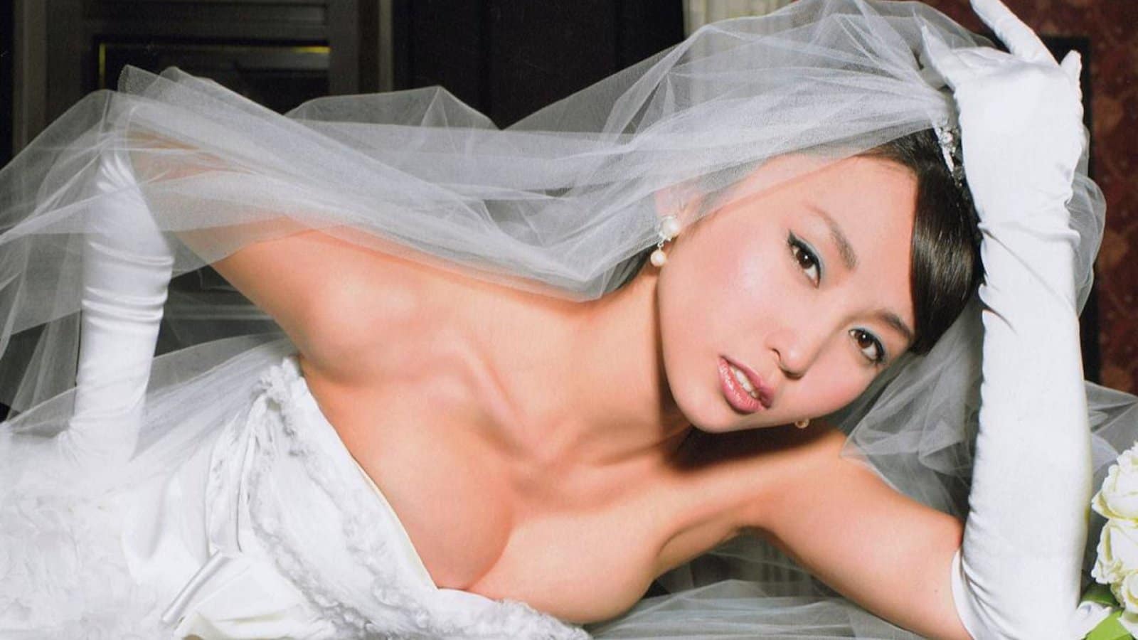 Alluring brunette Asian woman in a dress relaxing beautifully on a bed.